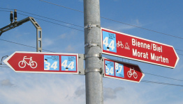 Corcelles: Route des Grands Longs Champs,
                          Wegweiser am Bahnbergang fr Velorouten