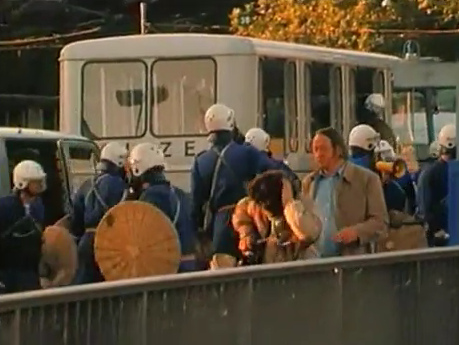 The criminal bully
                            policeman is turning away from his victim
                            and the hit woman is holding the location of
                            pain on her back of her head provoked by the
                            stroke of the bully policeman, Station Quay
                            (Bahnhofquai) in Zurich, evening of Sep. 4,
                            1980
