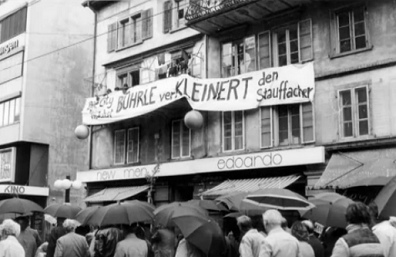 Squatted
                          houses at Stauffacher Square with the banner
                          "B�hrle makes the Stauffacher Square more
                          little" ("B�hrle verKleinert den
                          Stauffacher")